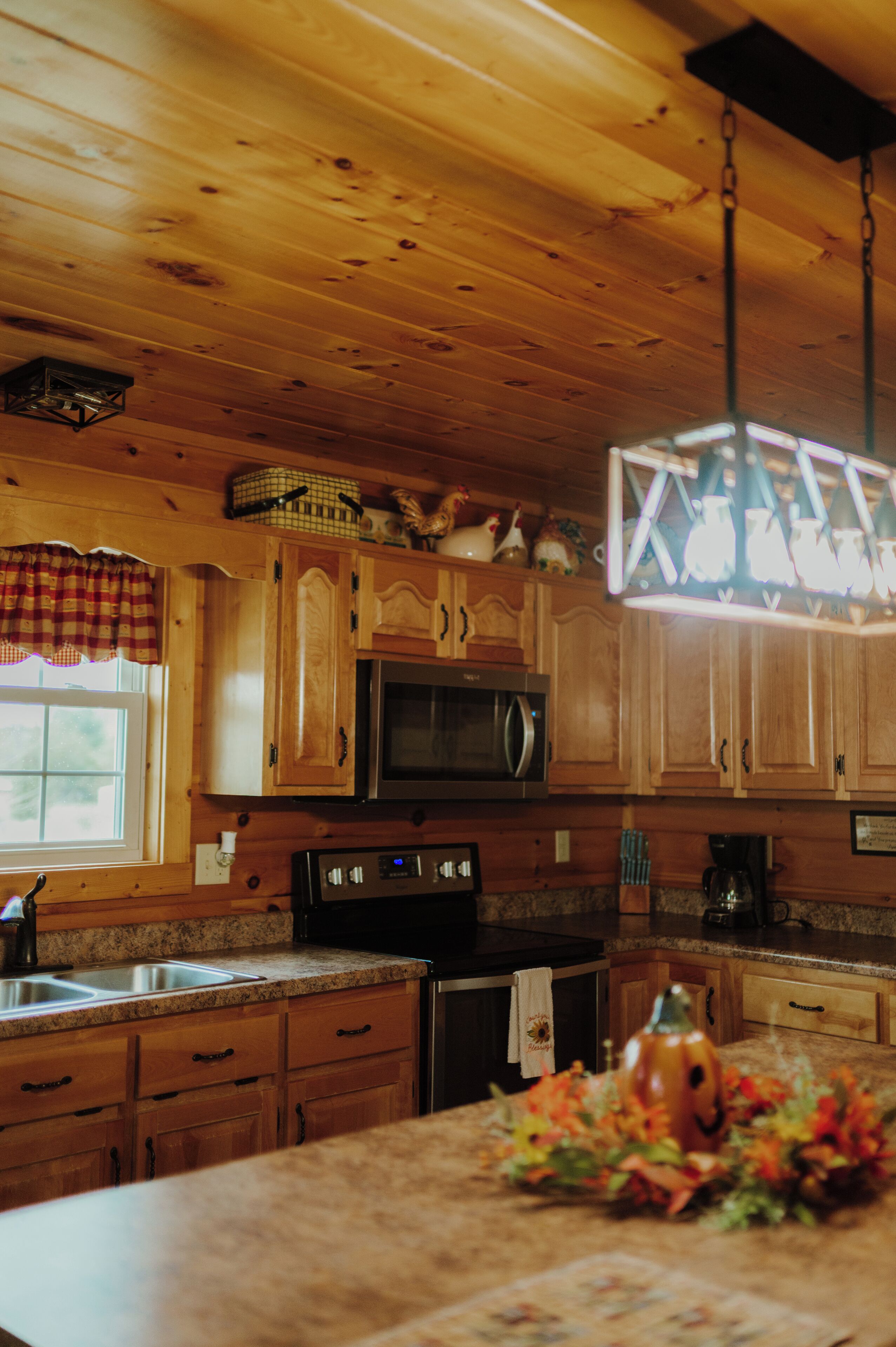 A wooden cabin interior with a kitchen featuring wooden cabinets, a microwave, stove, and a sink.