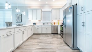 A modern kitchen with white cabinets, a stainless steel refrigerator, and a herringbone wood floor.