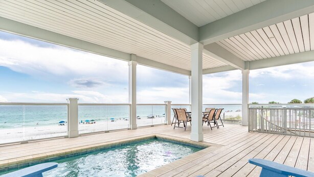 A covered outdoor area with a pool, wooden deck, and beach view.