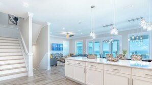 A spacious kitchen with a large island, white cabinetry, and a view of the ocean through large windows.