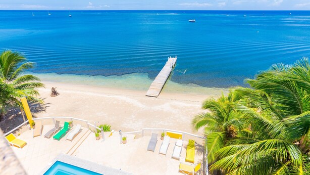 A beach view with a dock, lounge chairs, and a pool area.