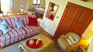 Una sala de estar acogedora con un sofá a rayas, una pequeña mesa redonda con un centro decorativo rojo, una silla y un mueble de madera.