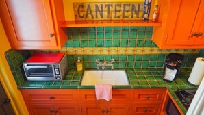 Una cocina con salpicadero de azulejos verdes, horno rojo, fregadero y cafetera.