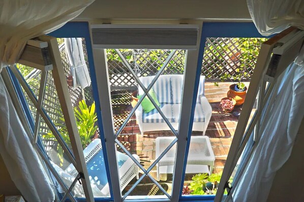 Vista a través de una ventana con un cerramiento de celosía, mobiliario exterior y plantas en macetas.