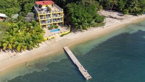 Un hôtel à plusieurs étages doté d’une piscine, situé sur une plage et comprenant une jetée qui s’avance dans l’eau.