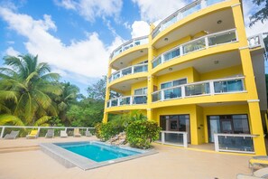 Un edificio giallo a più piani con balconi, piscina e palme.