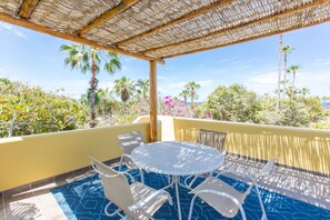 Un área de estar al aire libre cubierta con una mesa redonda y sillas, con vistas a una piscina y vegetación tropical.