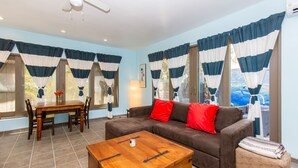Ein Wohnzimmer mit einem braunen Sofa, einem Holztisch, einem Esstisch mit Stühlen und gestreiften Vorhängen.