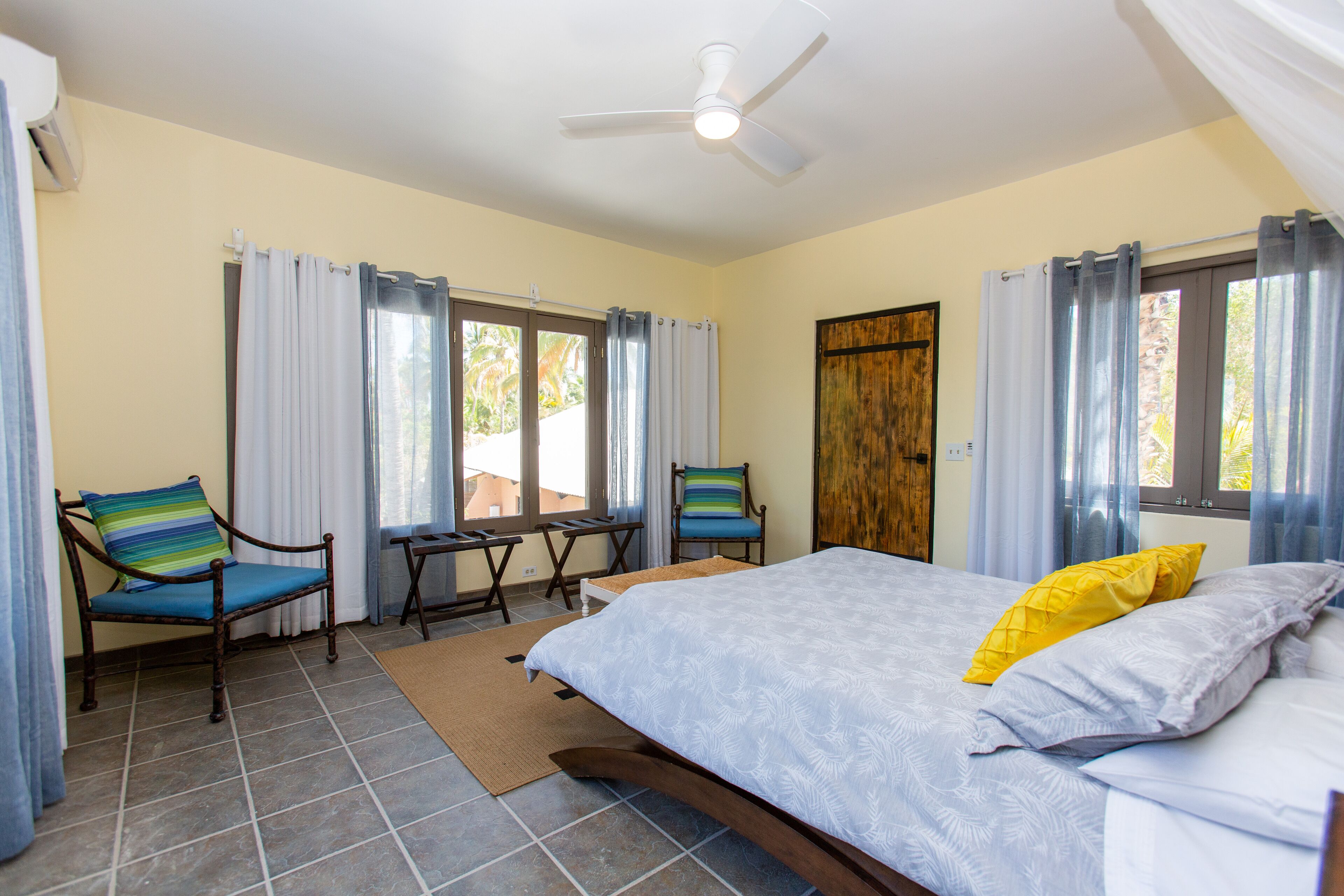 A bedroom with a bed, two chairs, a table, and a ceiling fan.