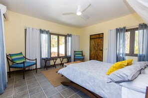 Un dormitorio con una cama, dos sillas, una mesa y un ventilador de techo.