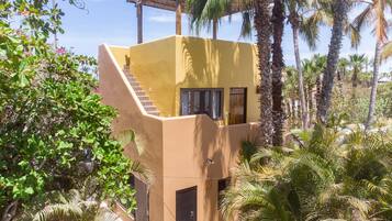 A two-story building with a staircase leading to the upper level, surrounded by lush greenery and palm trees.