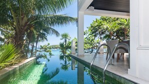 A pool with clear water, surrounded by tropical plants and overlooking a body of water.