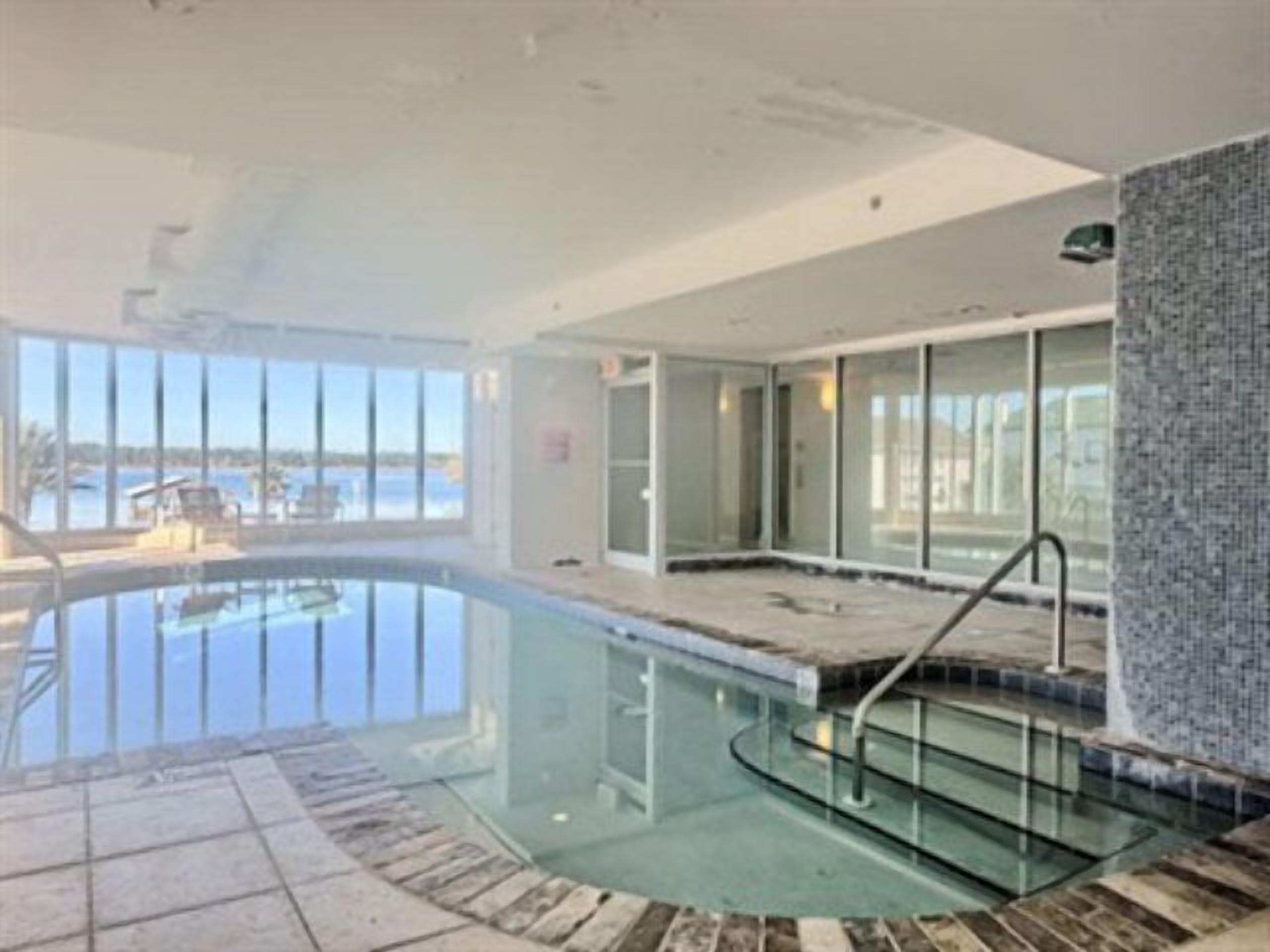 An indoor swimming pool with clear glass walls, a tiled deck, and a view of the water outside.