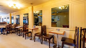 A restaurant interior with wooden tables and chairs, large windows, and a chandelier. - Woodlands Inn (Bangkok)