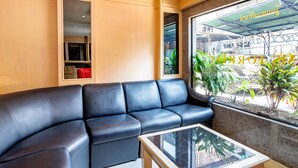 A modern hotel lobby with a black leather sofa, a glass-top coffee table, and a view of the street through a large window. - Woodlands Inn (Bangkok)