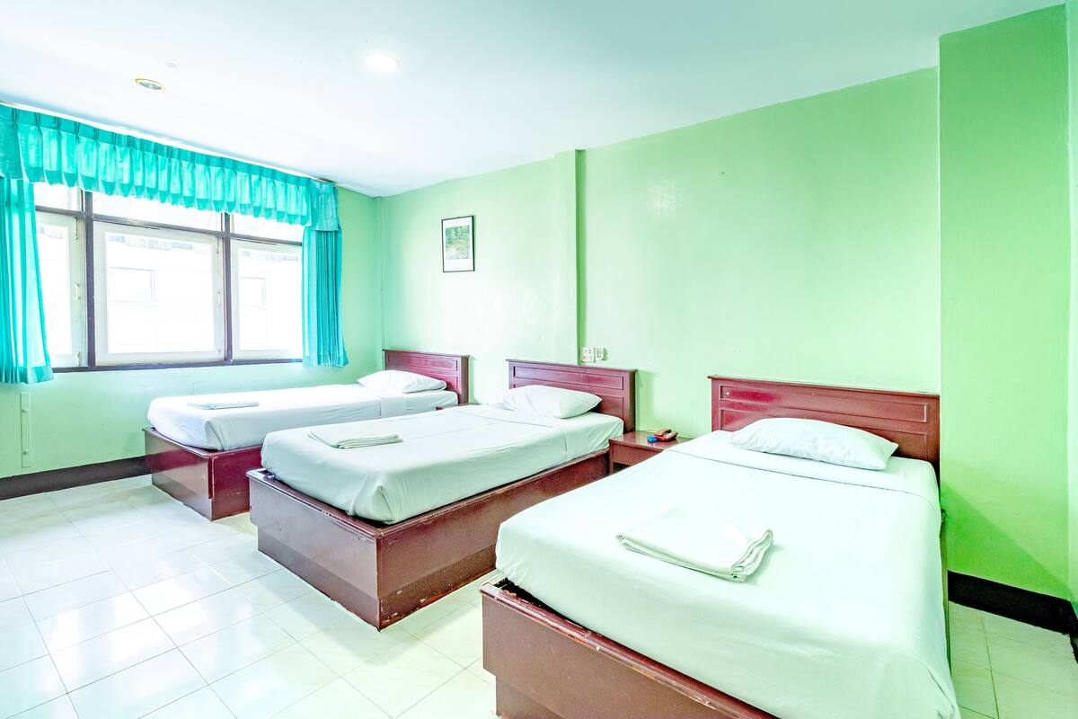 A hotel room with three single beds, a window with curtains, and a green wall.