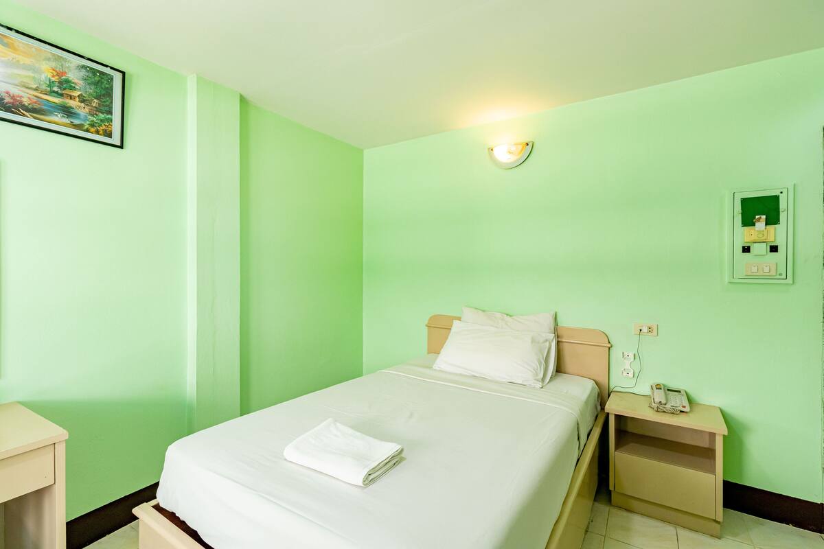 A room with a bed, a nightstand, a wall-mounted light, and a power outlet.