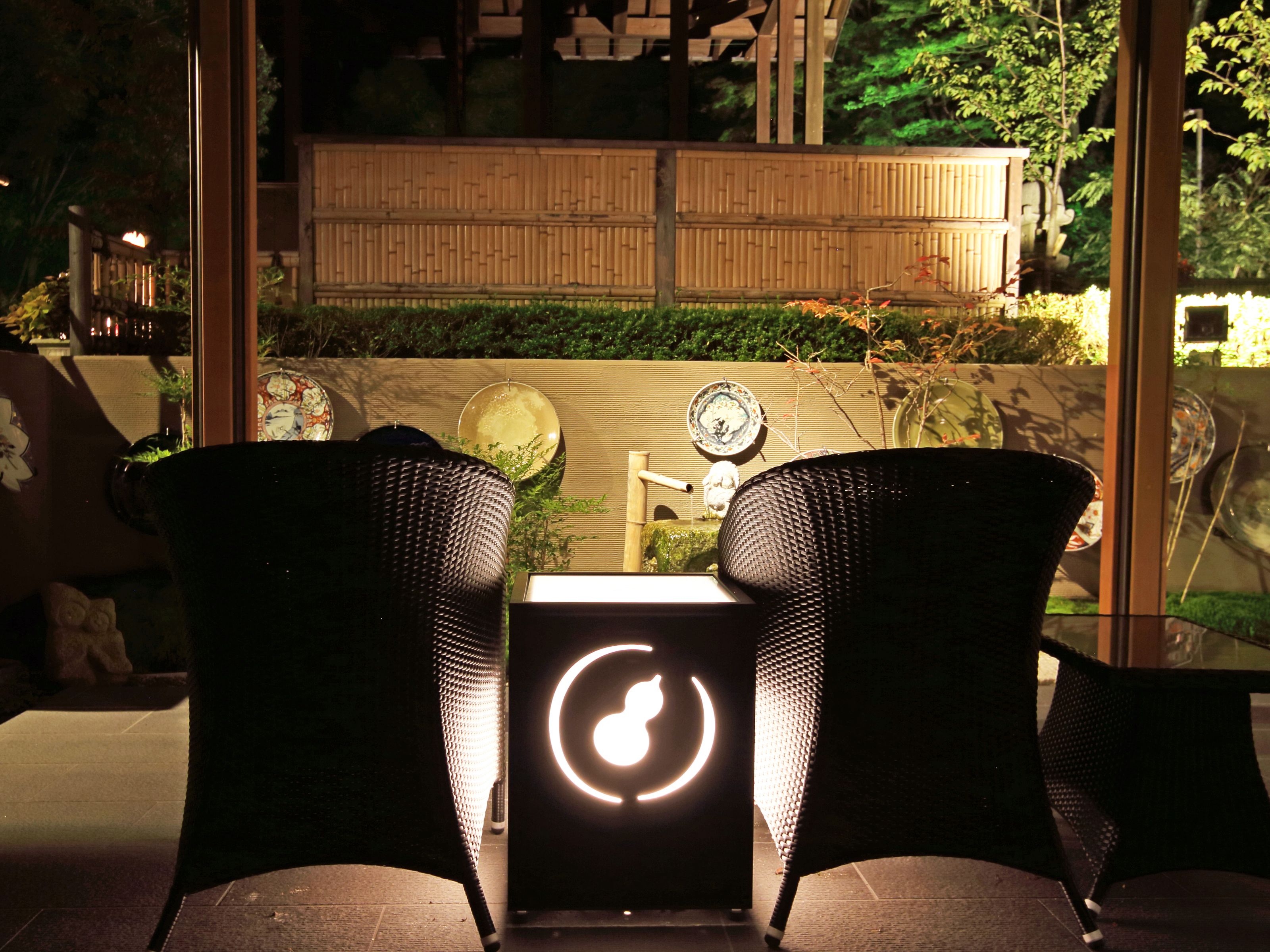 A seating area with wicker chairs and a table, a decorative wall with a bamboo fence, and a lit sign with a circular design.