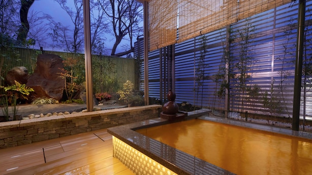 A modern outdoor area with a stone wall, a wooden deck, and a water feature. - Okuno Hosomichi (Kobe)