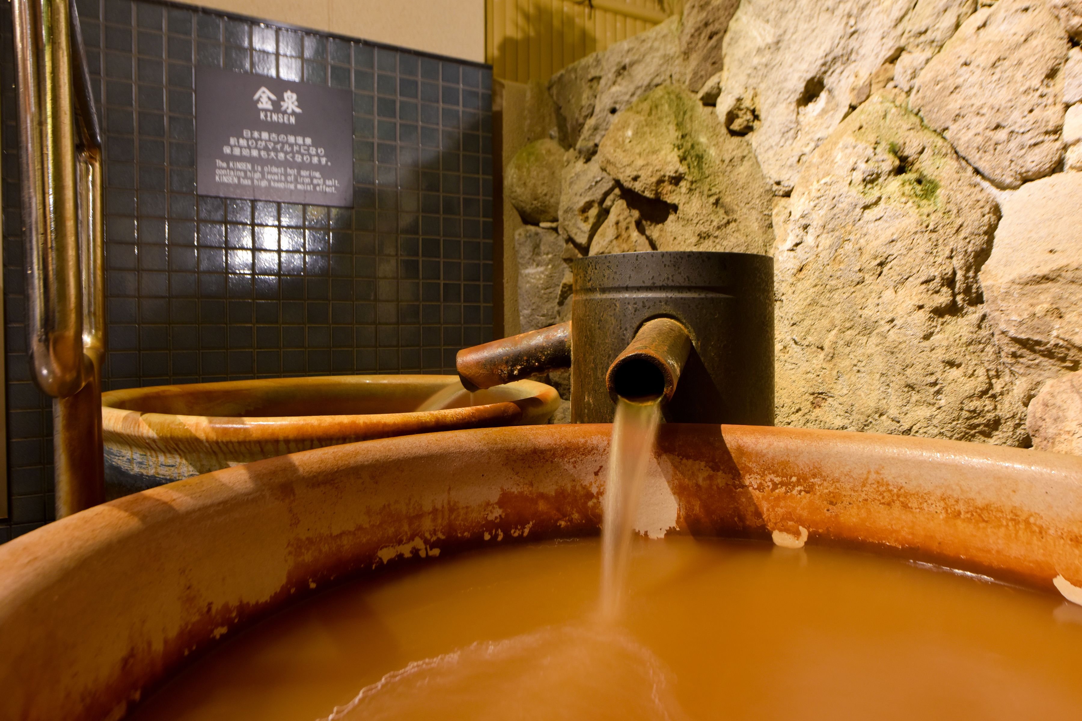 A traditional Japanese onsen with a stone wall and a sign in Japanese.
