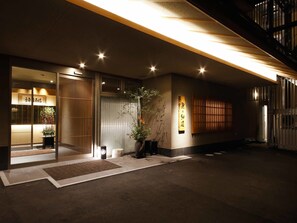 A modern building entrance with a wooden door, a potted plant, and a sign with Japanese characters.