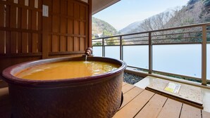 A large stone hot tub on a wooden deck with a view of a lake and mountains. - Okuno Hosomichi (Kobe)
