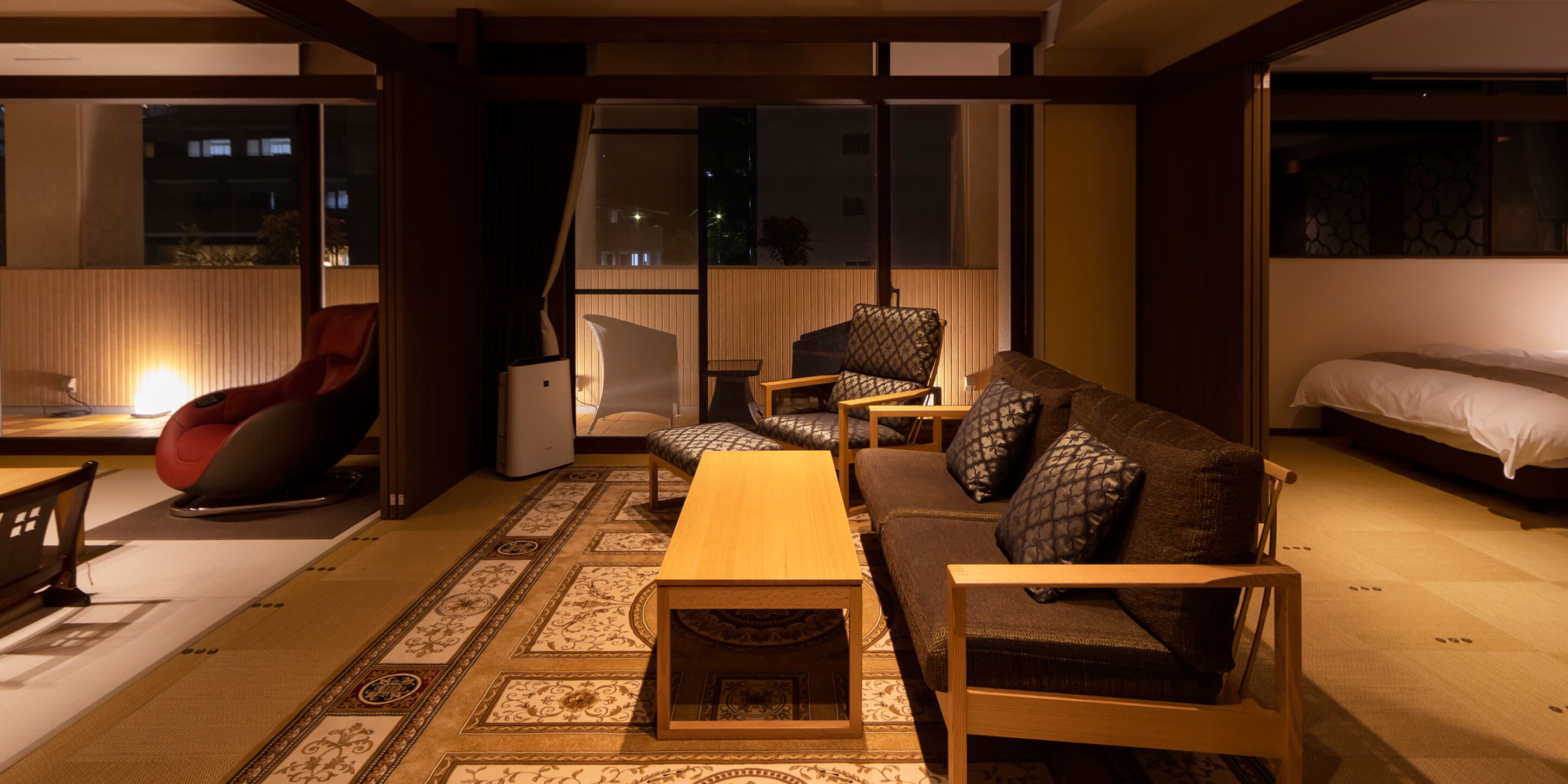 A modern living room with a sofa, chairs, a coffee table, and a bed.