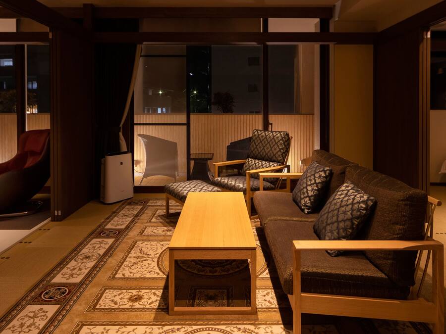 A modern living room with a sofa, chairs, a coffee table, and a bed.