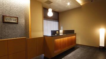 A reception area with a wooden counter, a tiled wall, and a ceiling with recessed lighting.