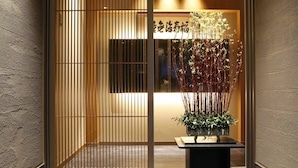 A traditional Japanese interior with a sliding door, a small table with a plant, and a sign with Japanese characters. - Okuno Hosomichi (Kobe)