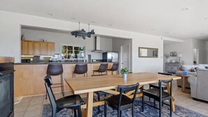 Een moderne keuken met een centraal eiland, een eethoek met een houten tafel en stoelen, en een zithoek met een bank en een televisie.