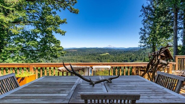 Een houten terras met een tafel en stoelen, met uitzicht op een bebost landschap en een berg in de verte.
