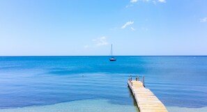 A wooden pier extending into a calm, clear blue sea with a sailboat anchored in the distance. - Villa Del Playa #1 (Roatan)