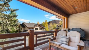 Un patio in legno con panchina e barbecue, affacciato su una montagna e una casa.