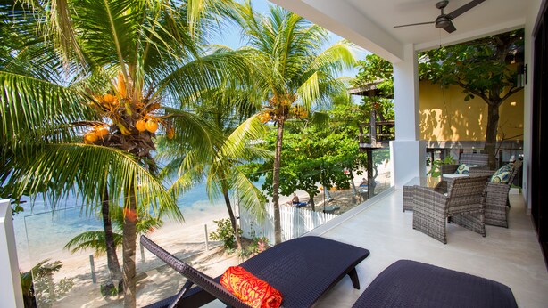 Ein Balkon mit zwei Liegestühlen, einem Deckenventilator und Blick auf den Strand und Palmen.