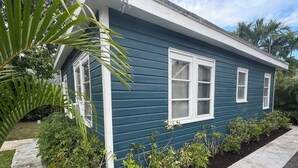 Ein blaues Haus mit weißen Verzierungen, umgeben von einem Garten mit verschiedenen Pflanzen und einem Betonweg.