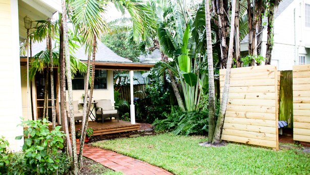 Ein Garten mit einem Ziegelweg, einer Holzdielen-Terrasse und verschiedenen tropischen Pflanzen.
