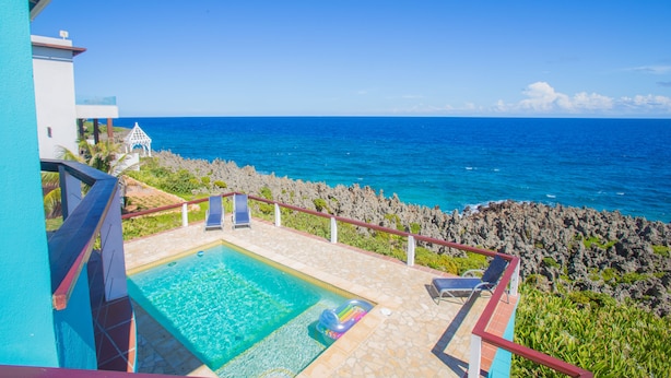 A pool area with a view of the ocean, a gazebo, and a rocky shoreline. - Stunning Coral View Home with Oceanfront Pool by RedAwning (Roatan)