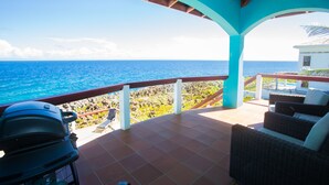 A covered outdoor area with a view of the ocean, a grill, and wicker furniture. - Stunning Coral View Home with Oceanfront Pool by RedAwning (Roatan)