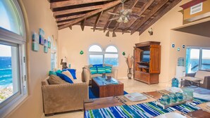 A living room with a view of the ocean, a wooden ceiling, and a sofa with cushions. - Stunning Coral View Home with Oceanfront Pool by RedAwning (Roatan)