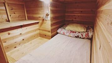 Una cabaña pequeña de madera con una cama individual y un banco.