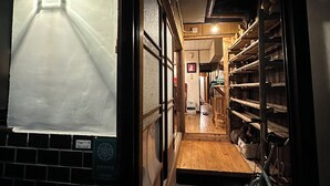 A narrow hallway with a wooden floor leading to a room with shelves and a bicycle. - Hostel Otro Mundo (Kyoto)