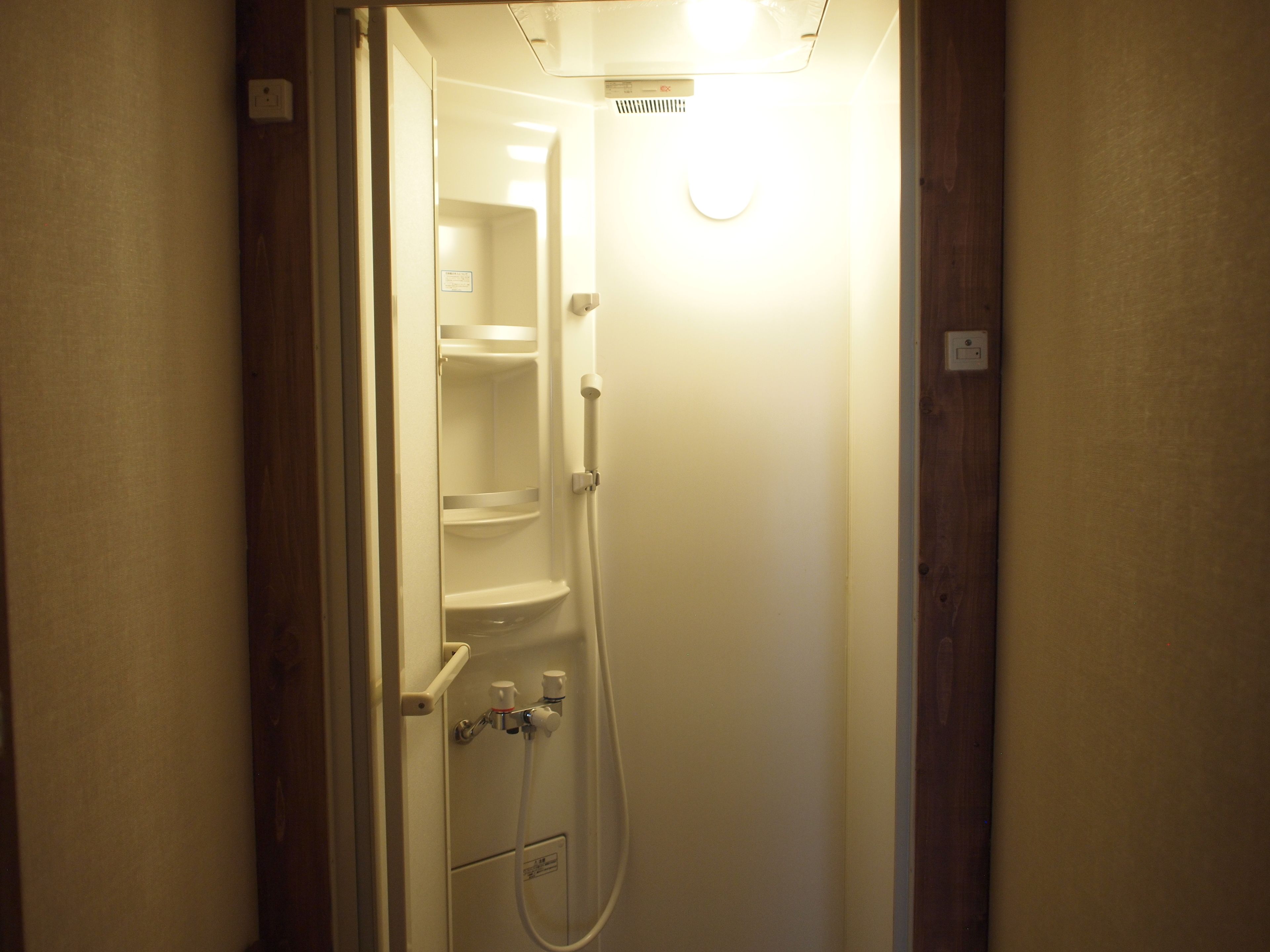 A small, enclosed shower area with a white sink and a handheld showerhead.