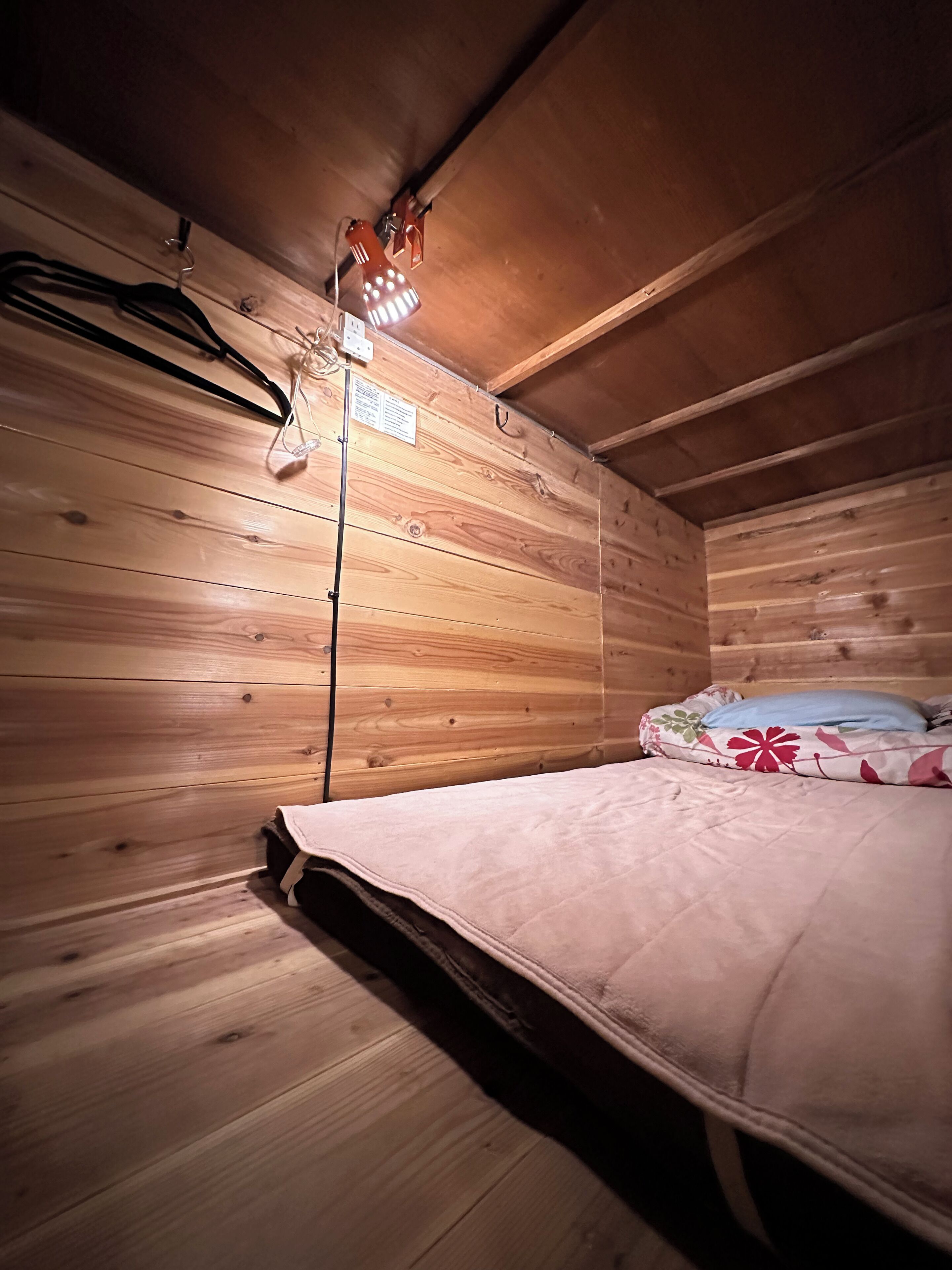 A wooden cabin room with a bed, a hanging light fixture, and a wooden ceiling.