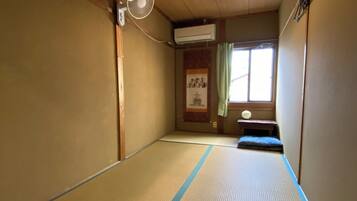 A tatami mat room with a ceiling fan, air conditioning, and a window with curtains.