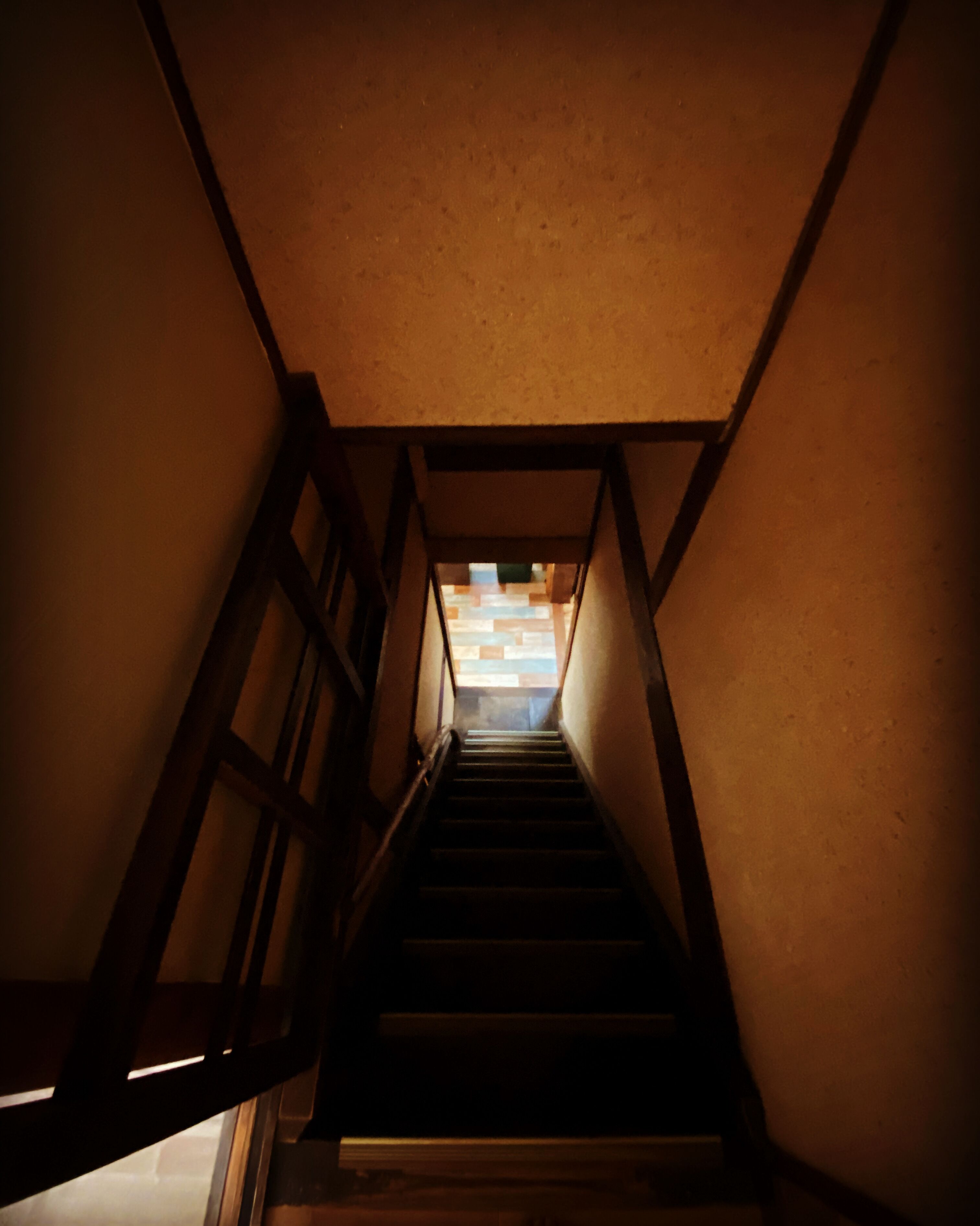 A narrow stairway with wooden railings leading to a bright area at the top.