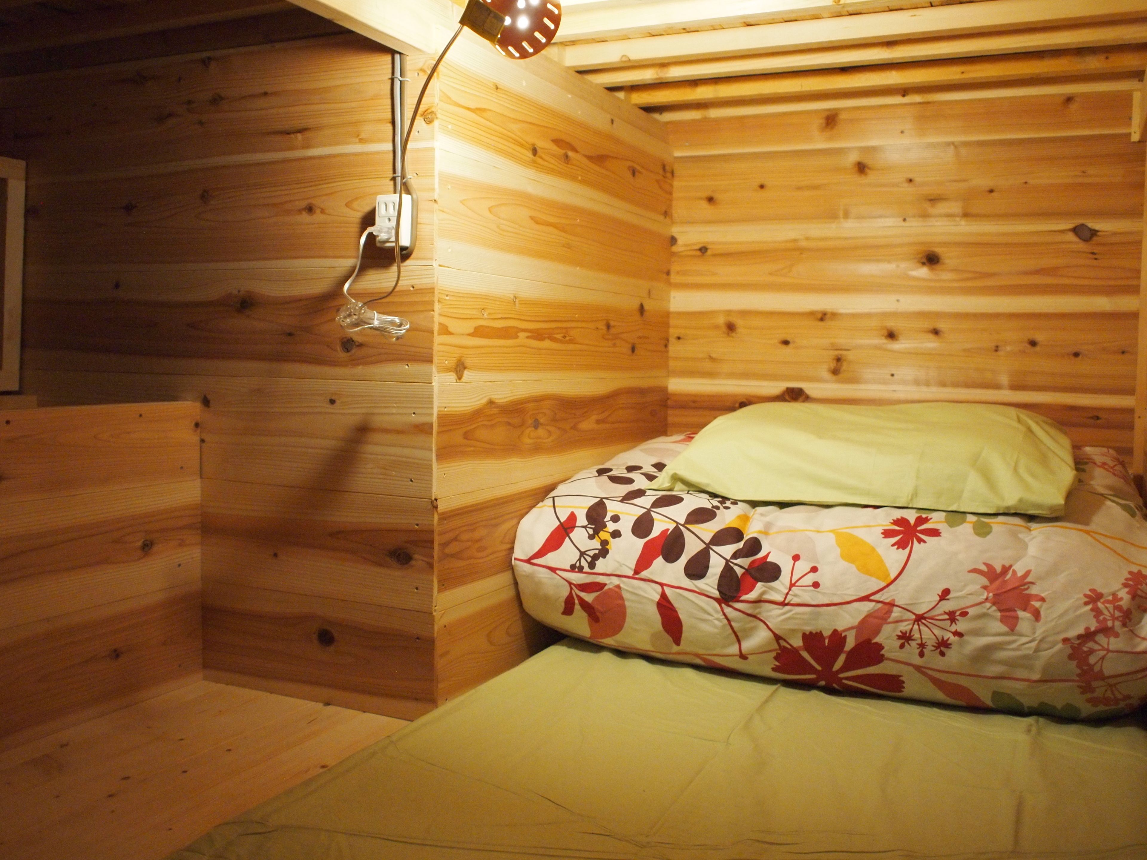 Una habitación de cabaña de madera con una cama, un enchufe y una lámpara en el techo.