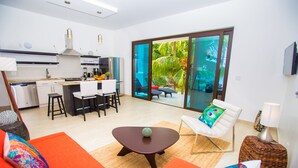 Un espace de vie moderne comprenant une cuisine, un coin repas et une grande porte-fenêtre coulissante donnant sur un jardin tropical.