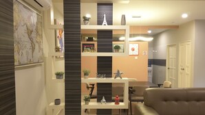 A modern living room with a sofa, a coffee table, and a TV. There is a bookshelf with decorative items and a map on the wall. - Laman Kurnia Holiday House (Kota Bharu)