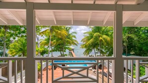 A covered outdoor area with a view of a beach and a pool. - Serenity Beach House (Roatan)
